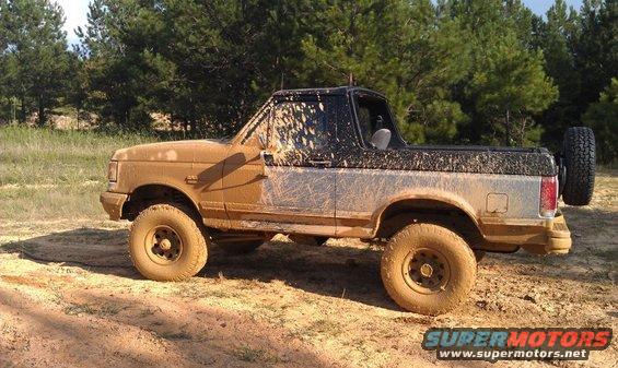 Mud-covered 1990 Ford Bronco parked on dirt with trees in background