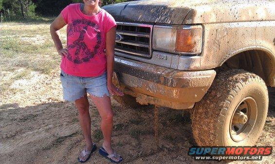 Woman in pink shirt and denim shorts stands next to a muddy Ford truck. Truck has a 4x4 badge