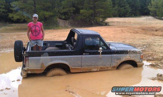 Two-tone gray and black Ford Bronco stuck in mud, spare tire mounted on rear