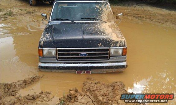 Front view of a muddy 1990 Ford Bronco stuck in mud
