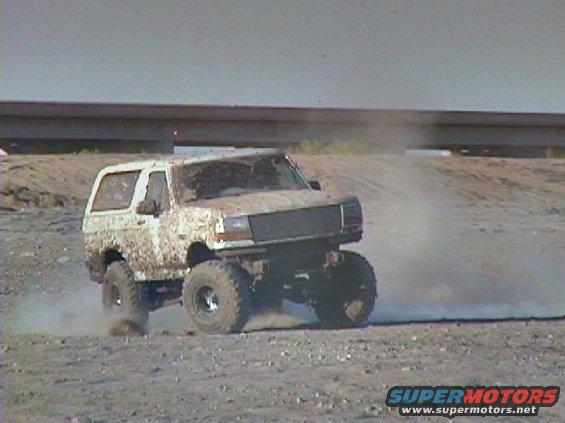 Mud-splattered white 1992 Ford Bronco driving off-road