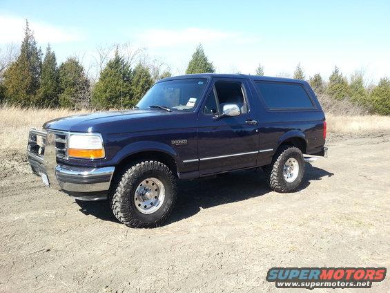 Dark blue Ford Bronco parked on a dirt road with trees in the background