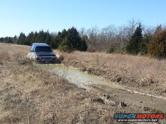 Dark blue 1995 Ford Bronco driving through mud