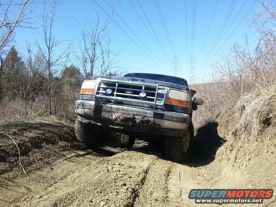 Black Ford Bronco on a dirt trail, front view, mud on grille and bumper