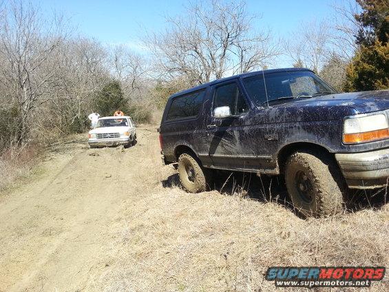 Dark blue SUV stuck in mud, front right wheel visible, other white SUV in background