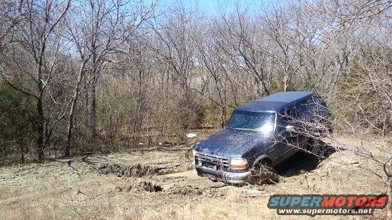 Blue 1995 Ford Bronco stuck in muddy terrain, front-left wheel deep in mud