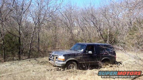 1995 Ford Bronco stuck in mud with trees in background
