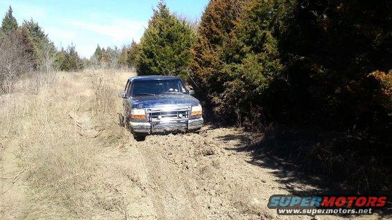 1995 Ford Bronco stuck in mud on a dirt track, surrounded by trees