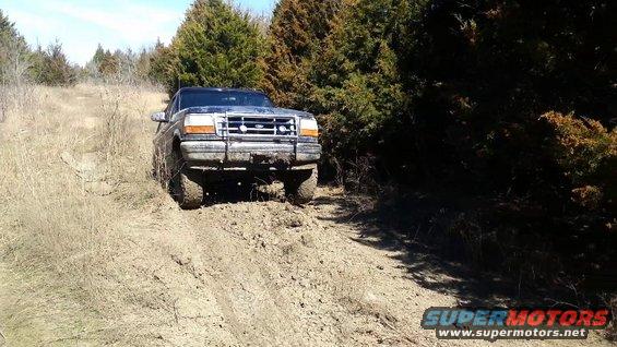 Ford Bronco driving up a muddy hill with trees around