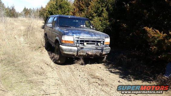 Blue Ford Bronco stuck in mud on a dirt path with trees in the background