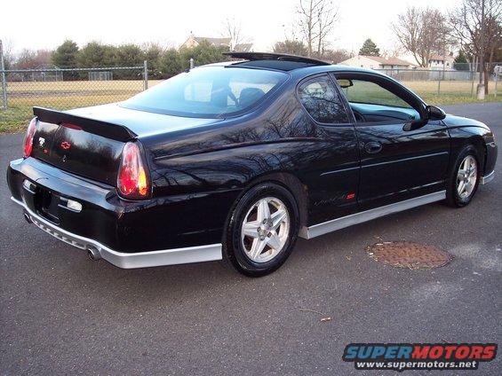 Black Chevrolet Monte Carlo SS parked on asphalt. It has a rear spoiler and silver trim along the bottom