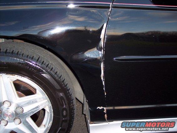 Black car fender and door with significant damage and rust around the seam