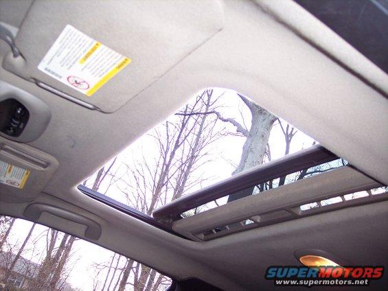 Car interior showing a sunroof open to bare trees and a cloudy sky