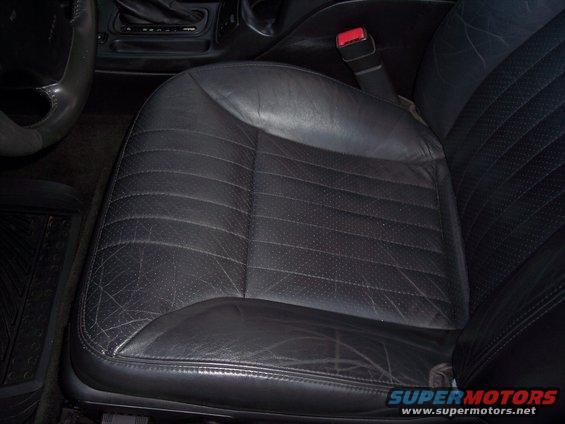 Black leather driver's seat with perforated inserts and visible wear, showing part of the steering wheel and center console