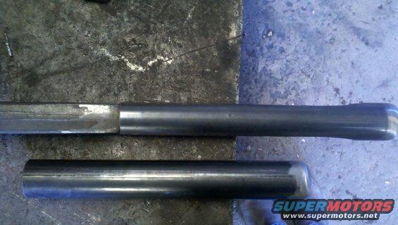 Two metal tubes, one longer and tapered, lie on a textured surface