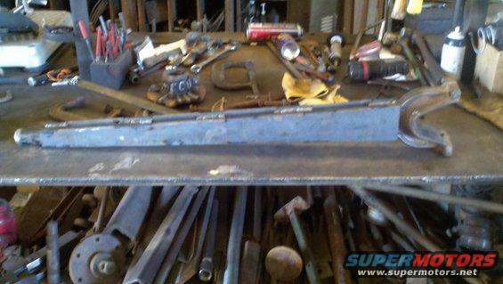 Metal part with a curved end on a cluttered workbench with tools