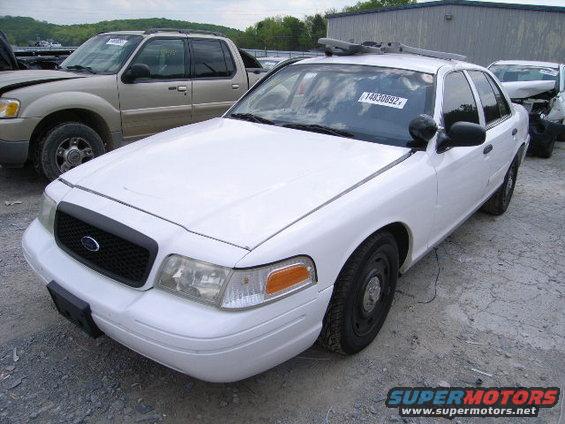 White 2003 Ford Crown Victoria police car parked next to a tan Ford Explorer. License plate 14830892 visible on windshield