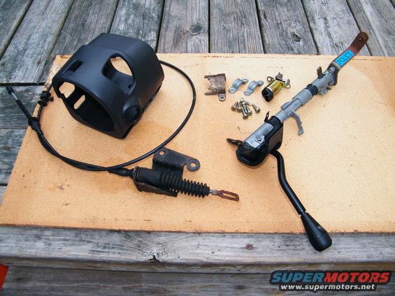 Steering column shroud, linkage, and assorted hardware laid out on a wooden surface. A blue label with 'POLICE' is visible on one part