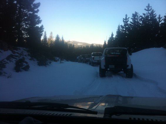Several off-road vehicles driving in a line on a snowy path through a forest