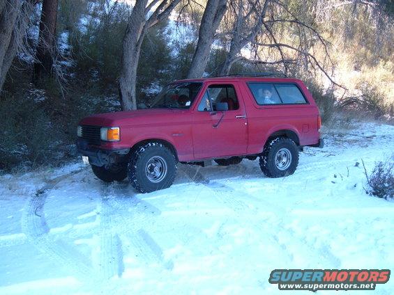 Red SUV with aftermarket wheels and tires in snow, front grille visible