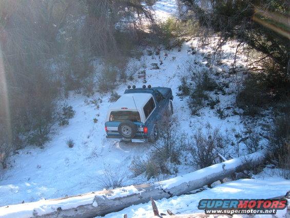 blue SUV with white top driving on a snowy hill, spare tire on back