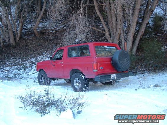 Red SUV parked in snow, rear view showing spare tire and trailer hitch