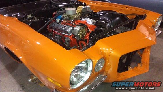 Orange 1970 Chevrolet Camaro front end with hood open, showing engine. Chrome bumper and headlights visible