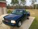 2000 GMC Sonoma - A dark blue 2000 GMC Sonoma pickup truck is parked on a concrete pad in front of a brick building.