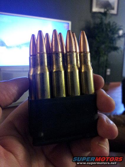 hand holds a black clip filled with brass cartridges and copper-tipped bullets