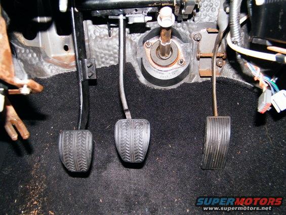 Car's three pedals: clutch, brake, and accelerator. Carpeted floor