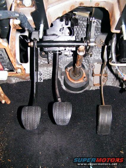 Three car pedals, including clutch, brake, and accelerator, with visible rust on mounting hardware