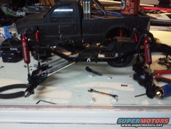 Black pickup truck chassis with red shock absorbers and suspension parts scattered around