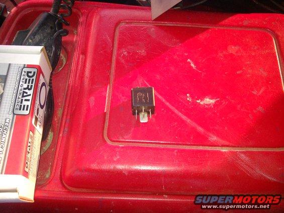 Automotive relay on red surface next to a box labeled 'DERALE PERFORMANCE'