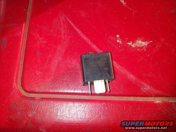 Black electrical relay with metal prongs on red textured surface