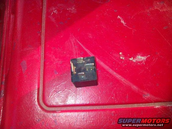 Black automotive relay with metal prongs on a red textured surface