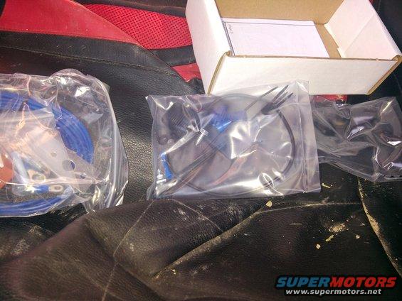 Parts in plastic bags on black and red car seats. A white box is open in the background