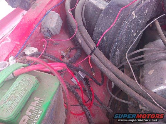 Engine bay with red fender, green battery, and red and black wiring. A grey electrical box is visible