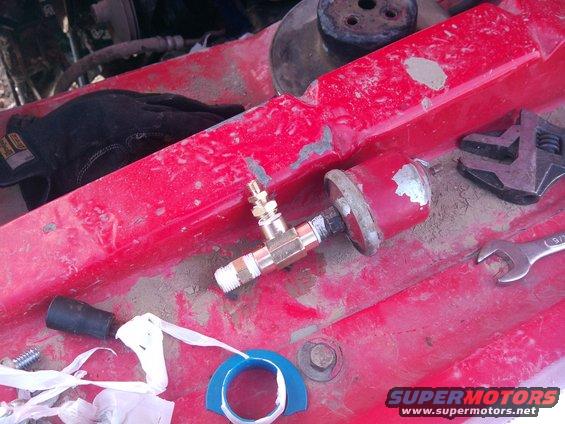 Engine bay with a red painted surface, a brass fitting with a valve, a black glove, and tools including a wrench