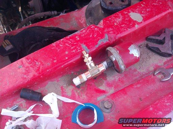 Close-up of a red engine bay with a pressure gauge, brass fittings, a black glove, and tools