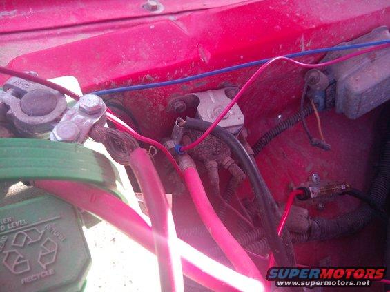 Close-up of red engine bay with battery terminals and wiring. Text on battery reads 'RECYCLE'