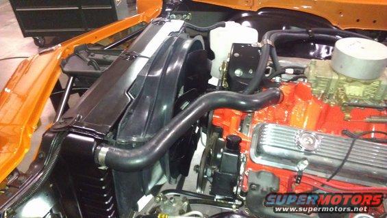 Engine bay showing radiator, fan, and orange painted engine block with chrome valve covers. Water pump and hoses are visible