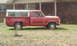 1987 Ford Bronco - A red pickup truck with a white camper shell is parked on a grassy area in front of a brick house.