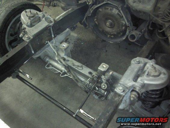 Close-up of a vehicle's frame, showing suspension components, steering rack, and part of the transmission