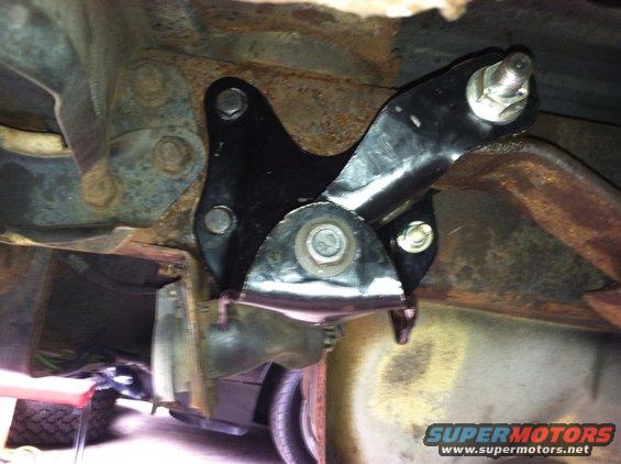 Undercarriage part with black metal bracket bolted to rusty frame. Tire visible