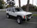 1994 Jeep Cherokee - A white 1994 Jeep Cherokee is parked in a lot, a roof rack and auxiliary lights on the roof.