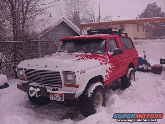 Red and white SUV parked outside in snowy weather. Roof rack visible on top