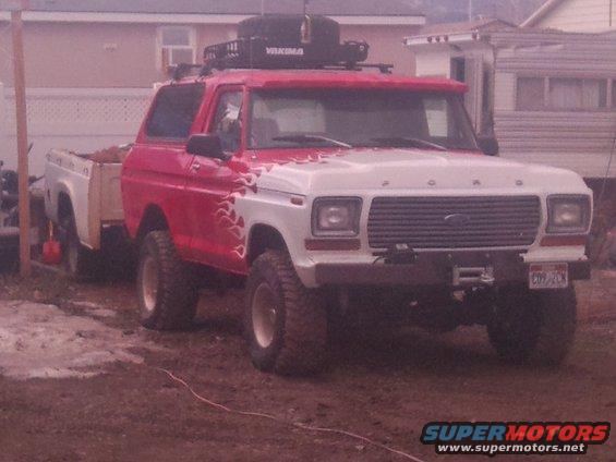 Red and white Ford Bronco with flames, Yakima roof rack, and a trailer behind it