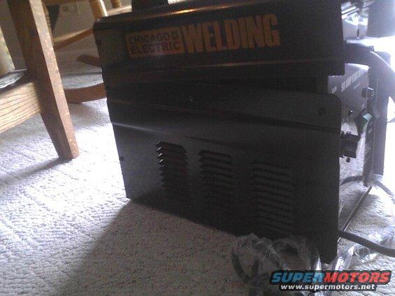 Black Chicago Electric welding machine on carpet, with wooden furniture in background