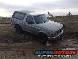 Gray Ford Bronco parked on dirt road with two people on bikes in background