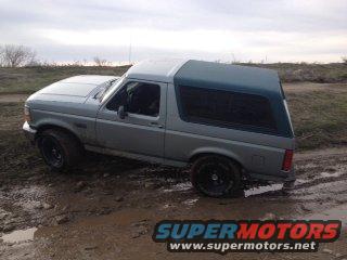 Gray Ford Bronco with a dark green canopy, stuck in mud, side view